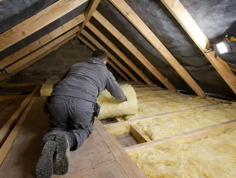 Installer laying mineral wool loft insulation between ceiling joists