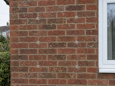 Old cavity insulation drill holes, filled with mortar, spaced across a brick wall